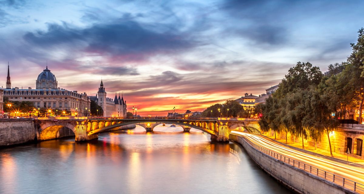 The Seine in Paris at sunset with a stone bridge and riverside lights, where many river cruises in France begin